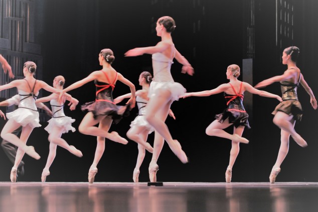A group of ballerinas doing pirouettes on stage, as seen from behind 